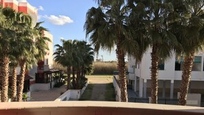 A balcony with a table set for two, overlooking a courtyard with palm trees and a building in the background. - Residence Massilor (Gallipoli)