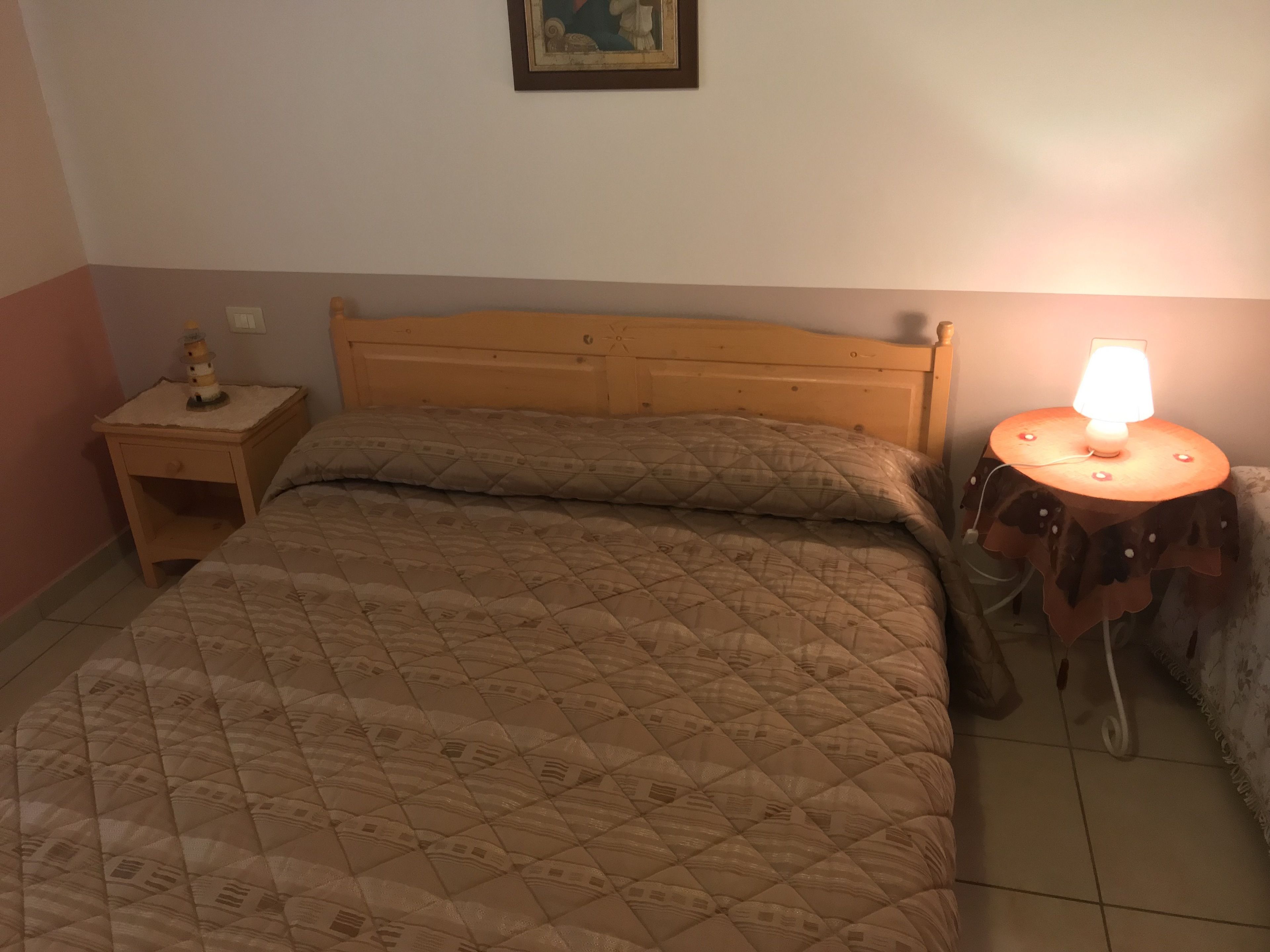 Une chambre à coucher avec un lit en bois, une table de chevet avec une lampe et une petite table également équipée d’une lampe.