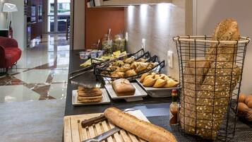A breakfast buffet with bread, pastries, and fruits.