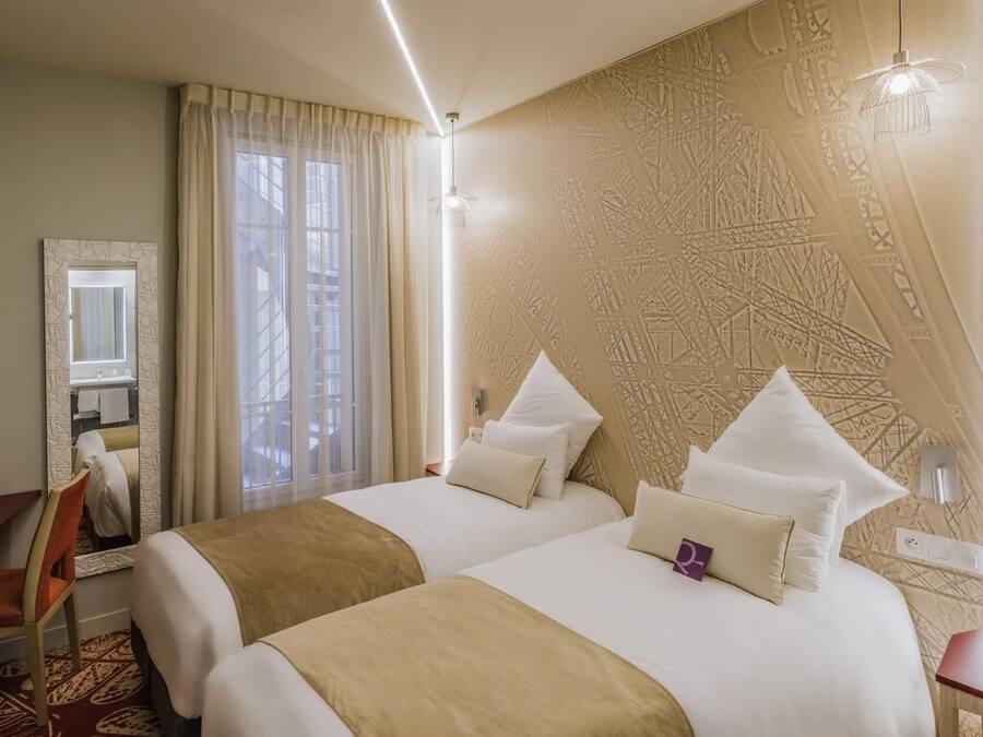 Une chambre d’hôtel avec deux lits, une grande fenêtre avec des rideaux, un miroir et un mur décoré d’un motif.
