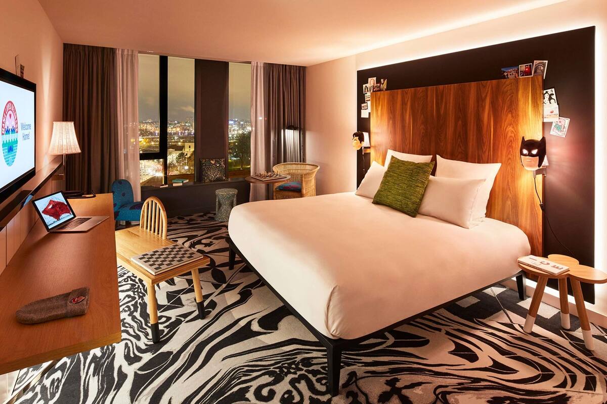 Ein Hotelzimmer mit Bett, Schreibtisch, Laptop, Stuhl, einem kleinen Tisch und Blick auf die Stadt.