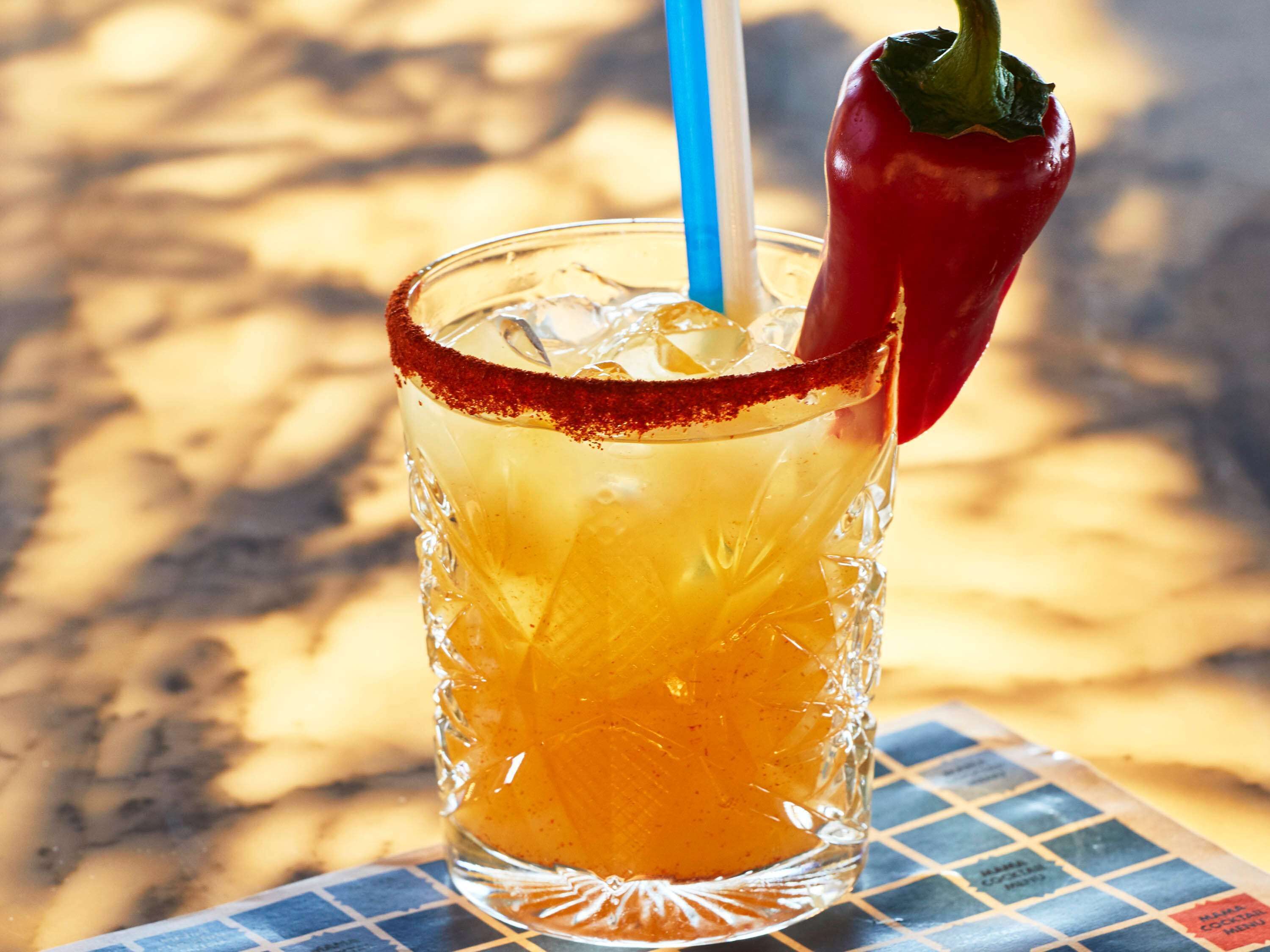 A glass with a red rim, ice cubes, and a red chili pepper on the rim.