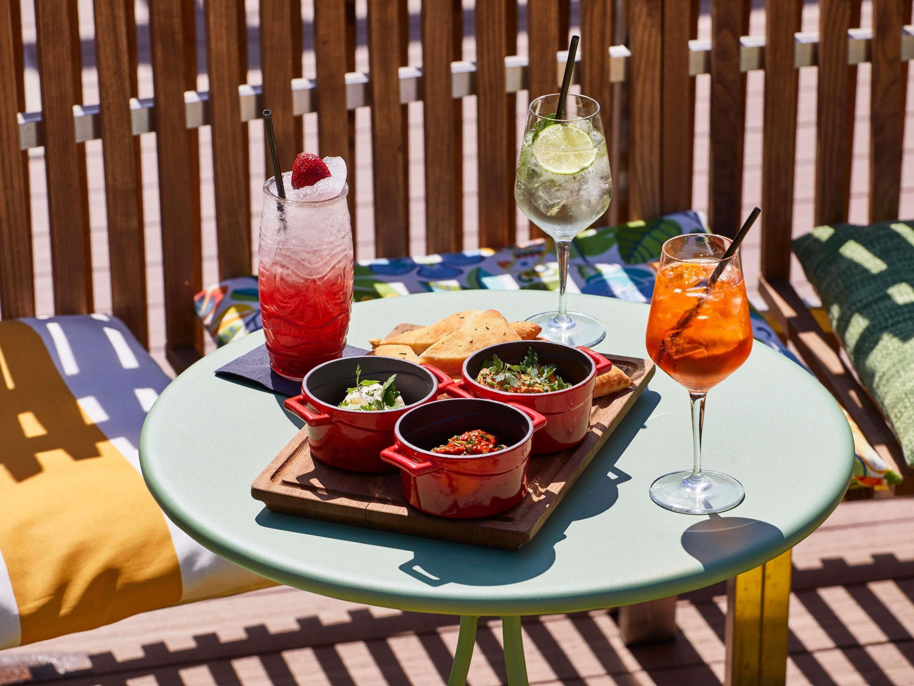 A table with food and drinks, a wooden fence in the background, and a colorful cushion.