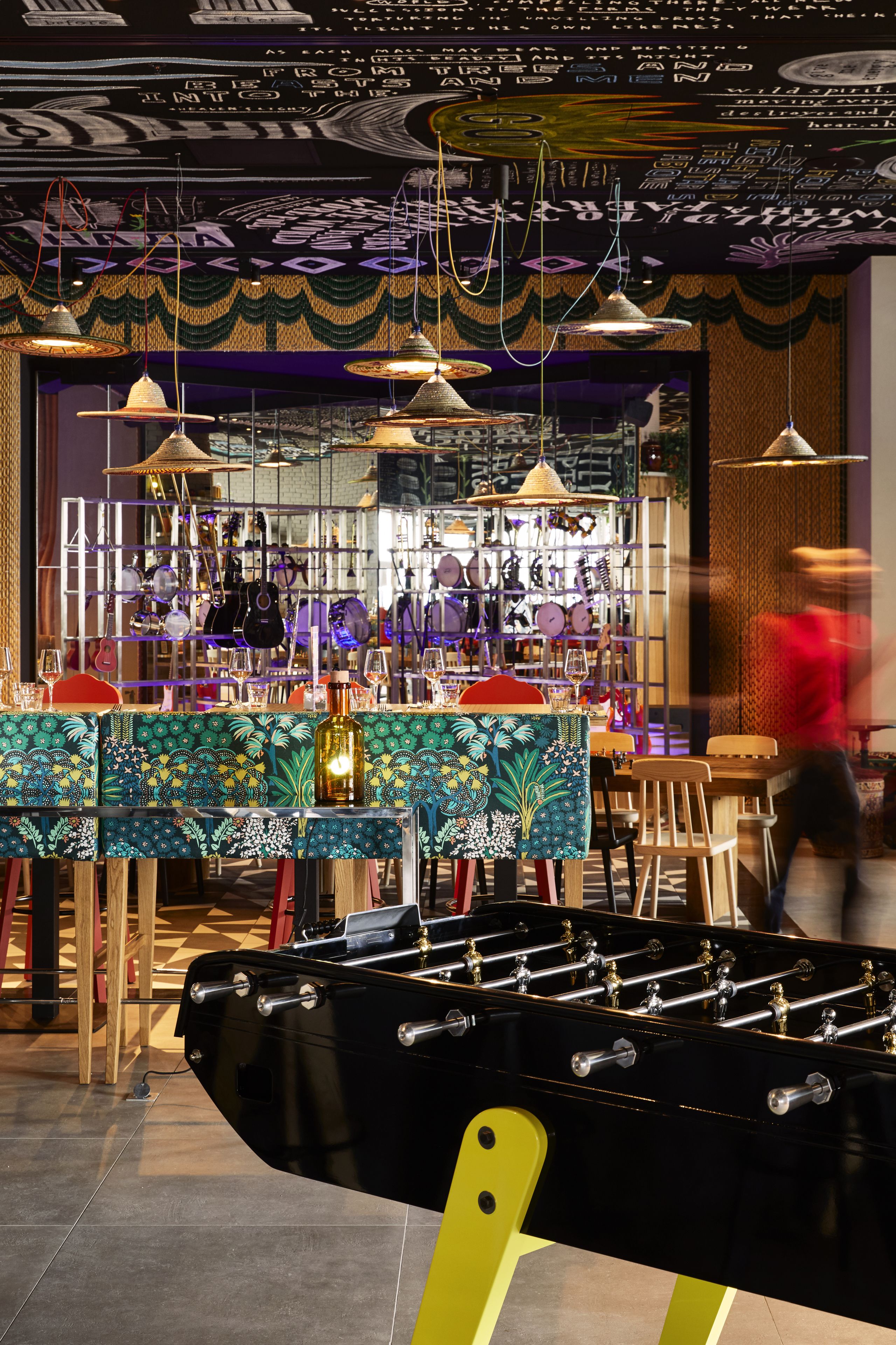 A room with a foosball table, a bar area with various items on shelves, and hanging lights.