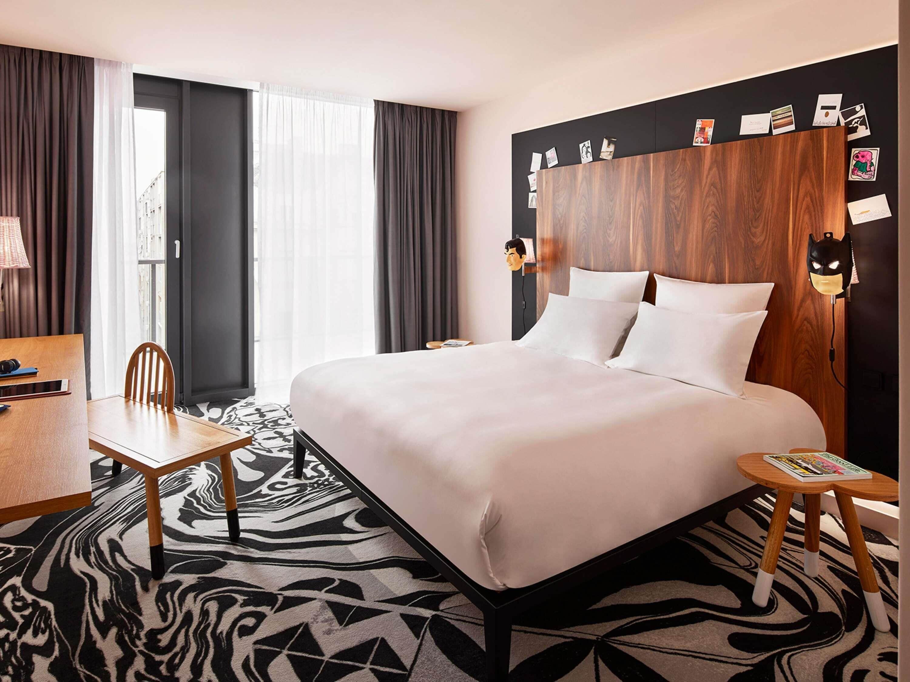 Habitació d'hotel amb un llit, un escriptori, una cadira, una catifa amb estampat de zebra i una paret amb fotos i una mascareta de Batman.
