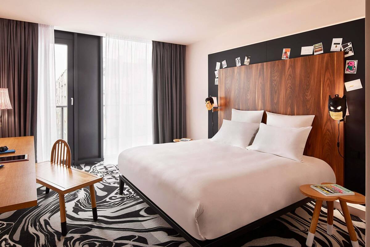 Ein Hotelzimmer mit Bett, Schreibtisch, Stuhl, einem Zebra-Teppich und einer Wand mit Fotos und einer Batman-Maske.