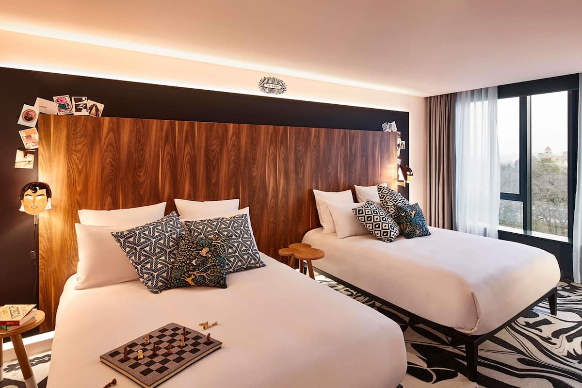 Ein Hotelzimmer mit zwei Betten, einem hölzernen Kopfteil, einem Schachbrett auf dem Bett links und einem Teppich mit ZEBRA-Muster.