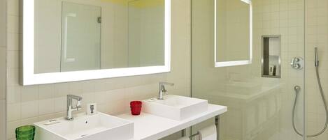 A bathroom with two sinks, a large mirror, a glass shower enclosure, and a towel rack.