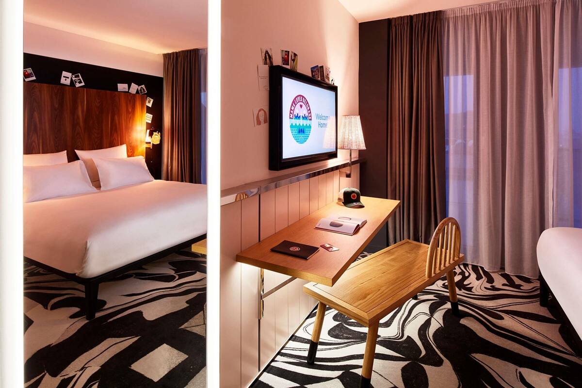 Ein Hotelzimmer mit Bett, Schreibtisch mit Stuhl, Fernseher und einem Fenster mit Vorhängen.