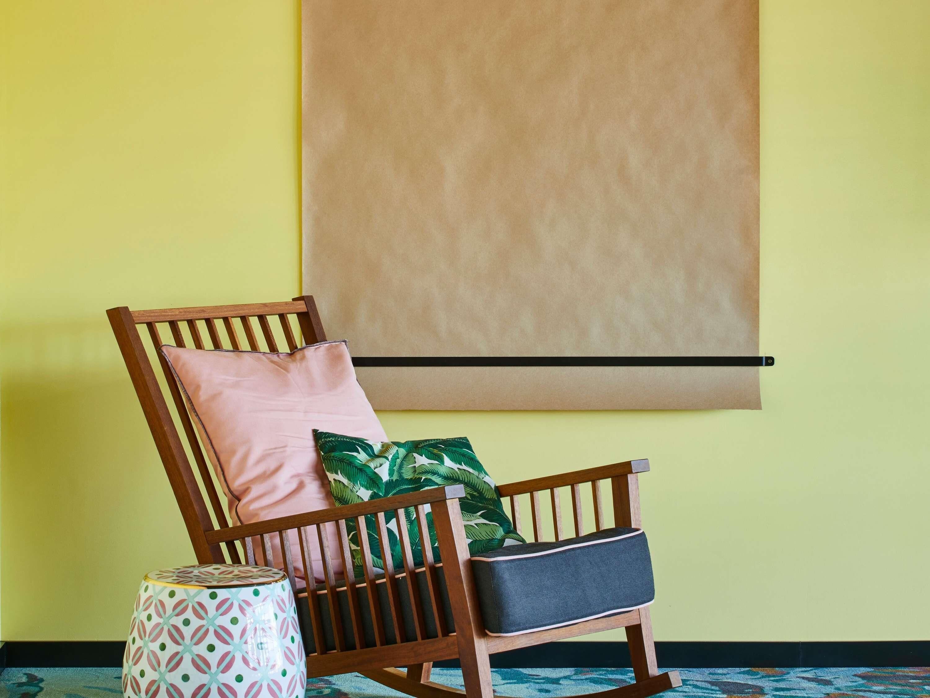 A wooden chair with a cushion, a small round table with a patterned top, and a plain wall with a horizontal line.