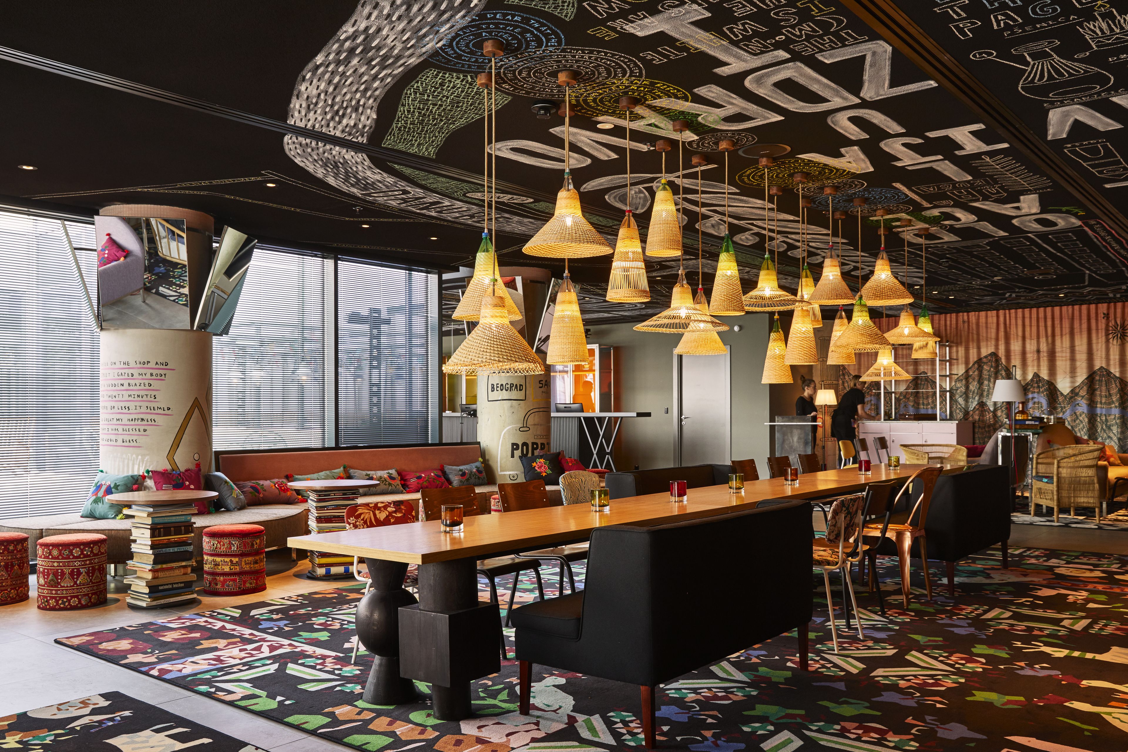 A modern interior with a long wooden table, black chairs, and hanging wicker lamps.