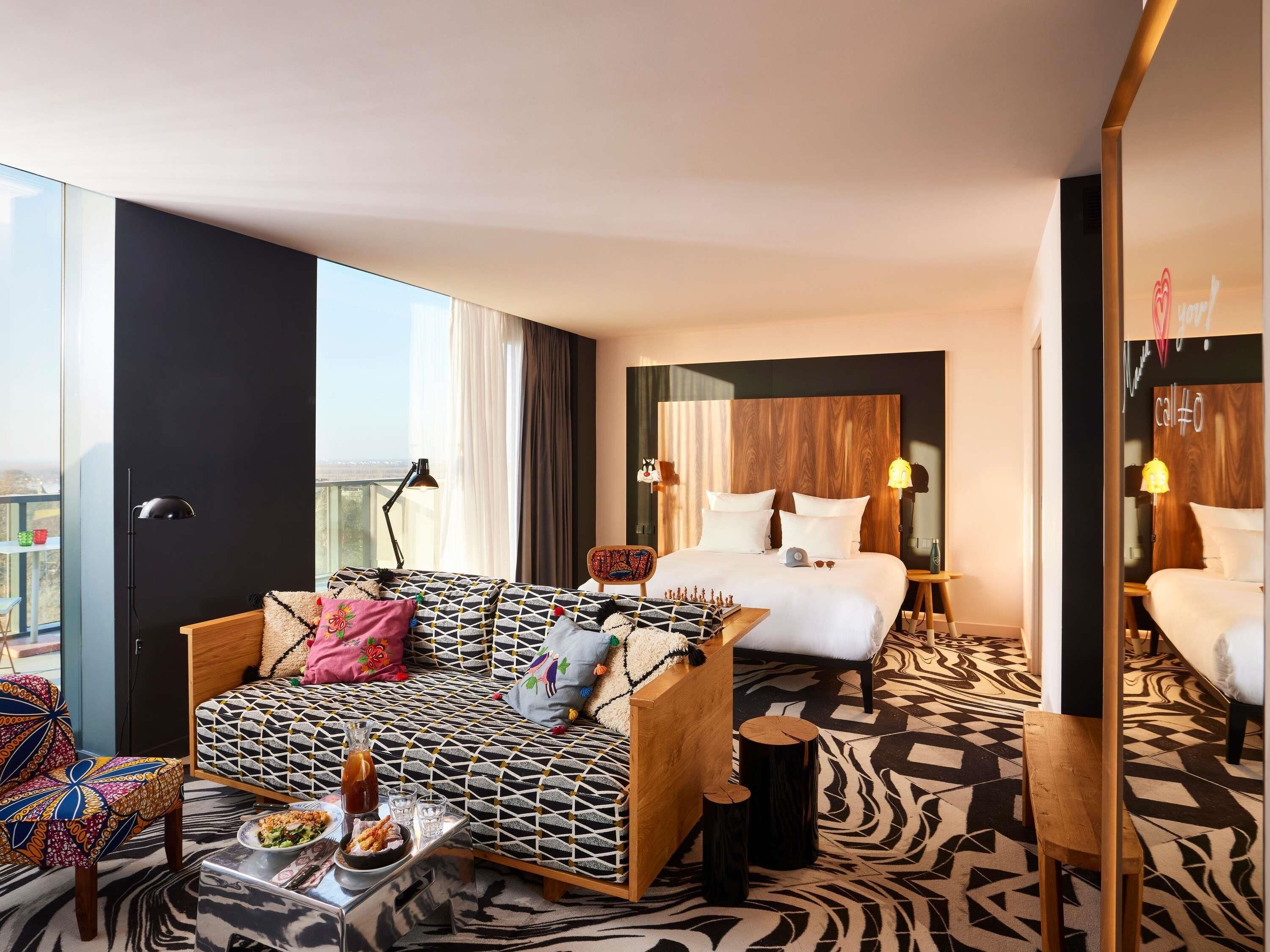 Una habitación de hotel con sofá, cama, mesa de comedor con comida y vistas a la ciudad.