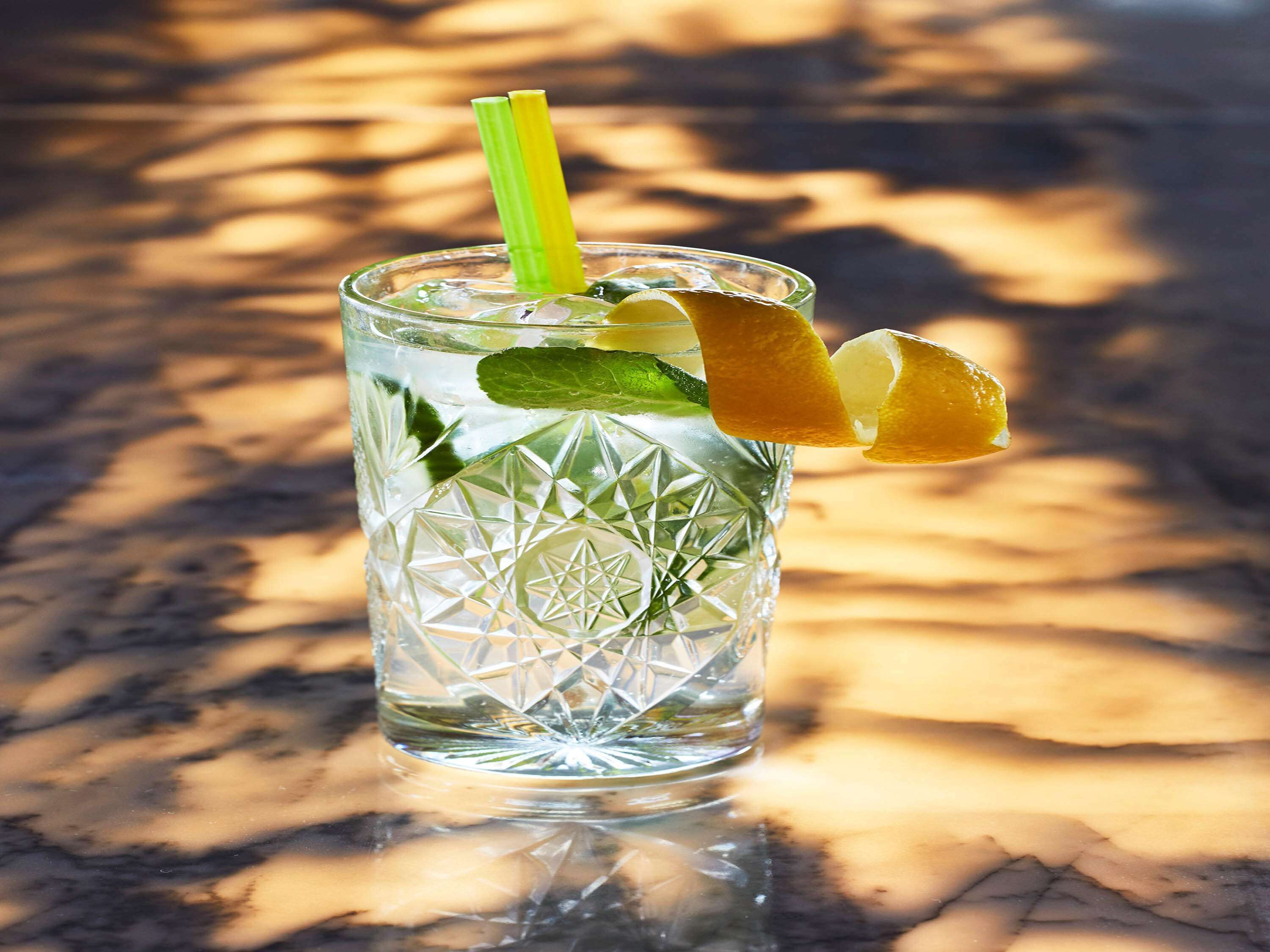 Un vaso transparente con un diseño geométrico, conteniendo una bebida adornada con una cuña de limón y una rodaja de lima, y una pajita verde.