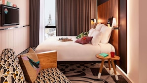 A hotel room with a large bed, a TV, a view of a cityscape, and a small table with a book and a glass. - Mama Shelter Belgrade (Belgrade)