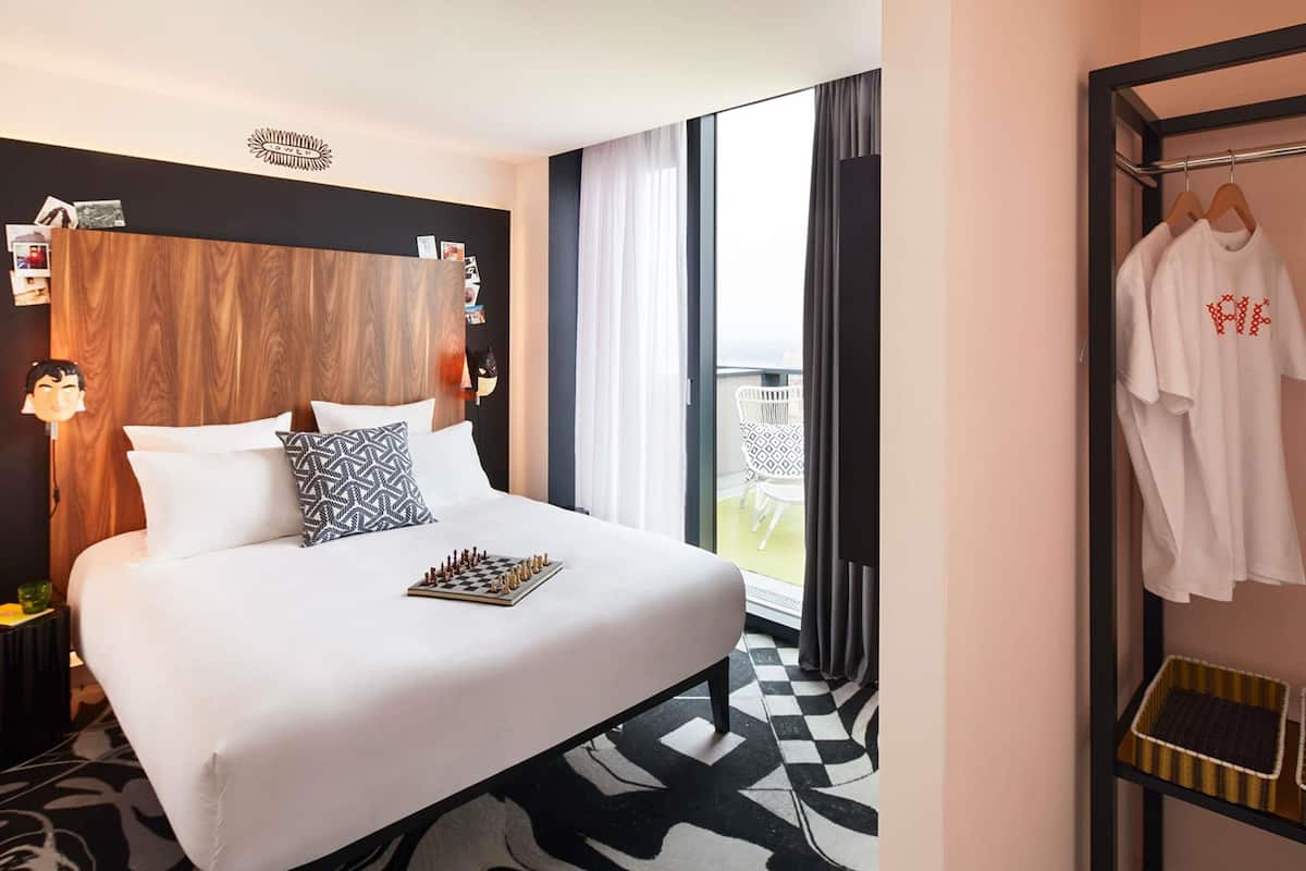 Ein Hotelzimmer mit einem großen Bett, einem Schachbrett, einem Kleiderschrank und einem Balkon mit Sitzgelegenheit.