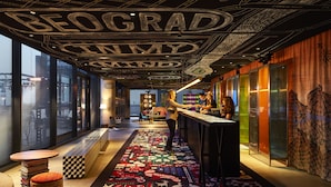 A modern bar area with a checkered floor, a bar counter, and a ceiling with large letters spelling out a name. - Mama Shelter Belgrade (Belgrade)