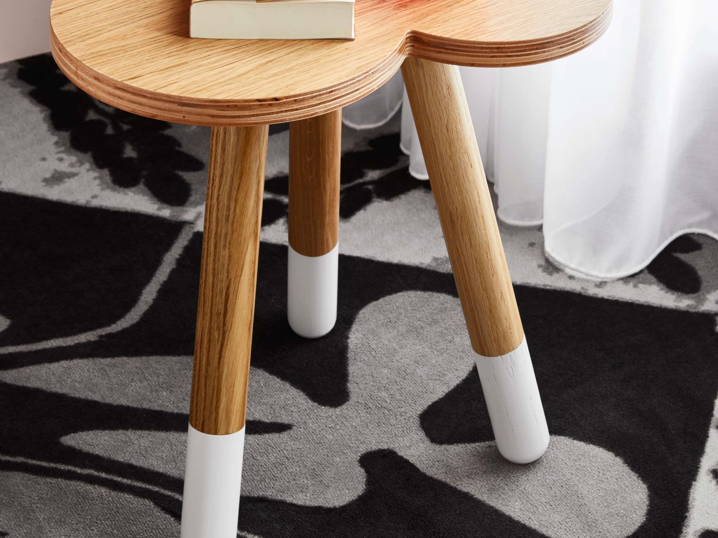 Una mesa redonda de madera con un libro encima, dos patas de madera con bases blancas y una alfombra de estampado blanco y negro.