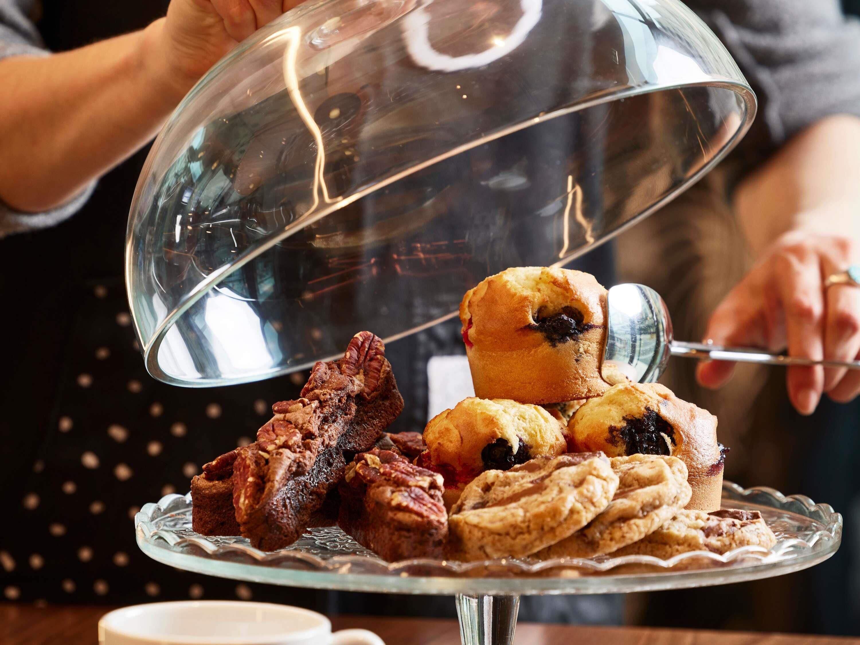 A dessert display with a glass dome cover, including pastries and cookies.