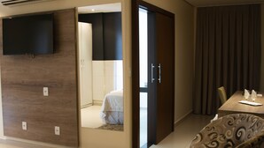 A modern hotel room with a flat-screen TV, a bed, a dining area with a table and chairs, and a large mirror. - Golden Plaza Hotel by Easy Class (Porto Velho)