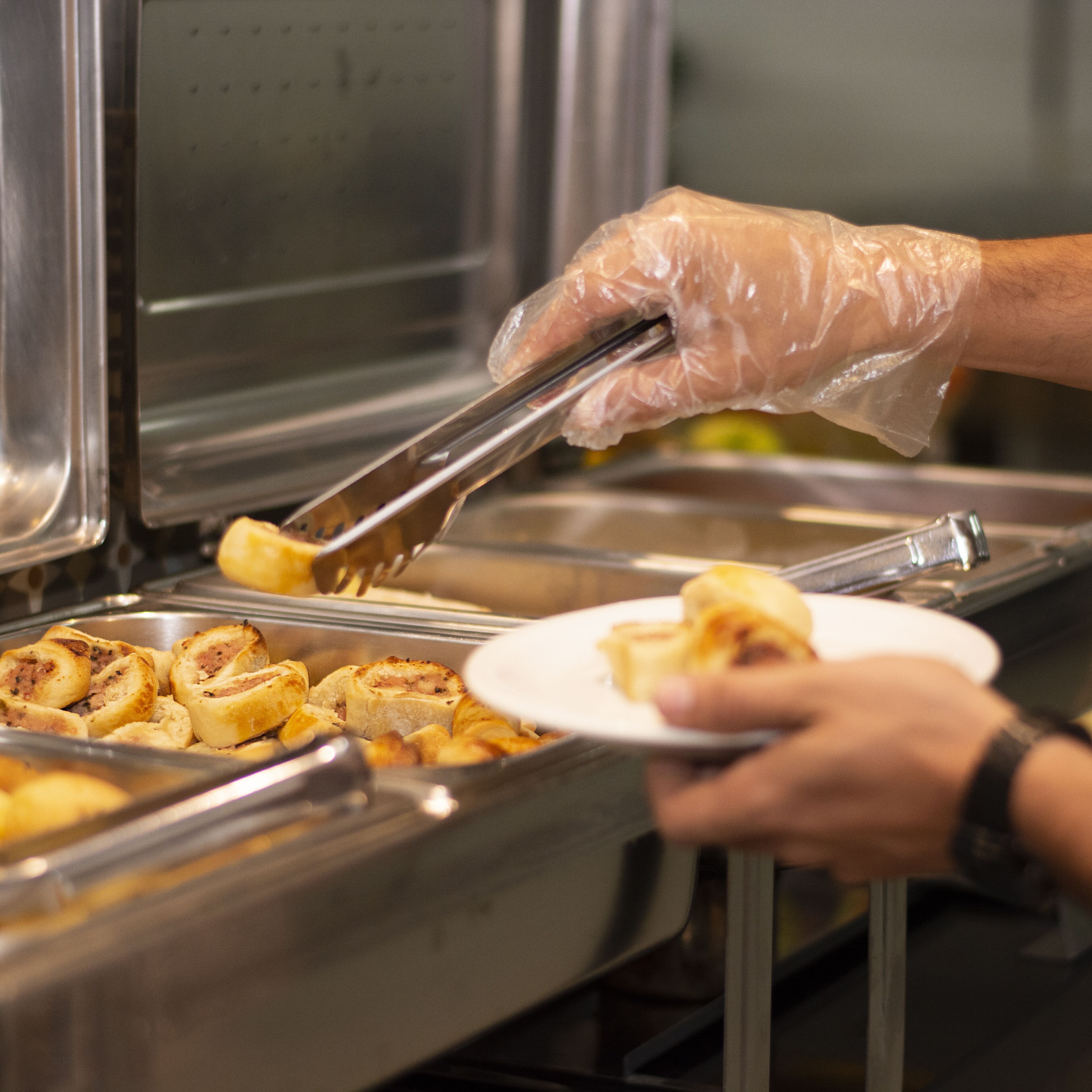 Un buffet con una persona che serve cibo con delle pinze.