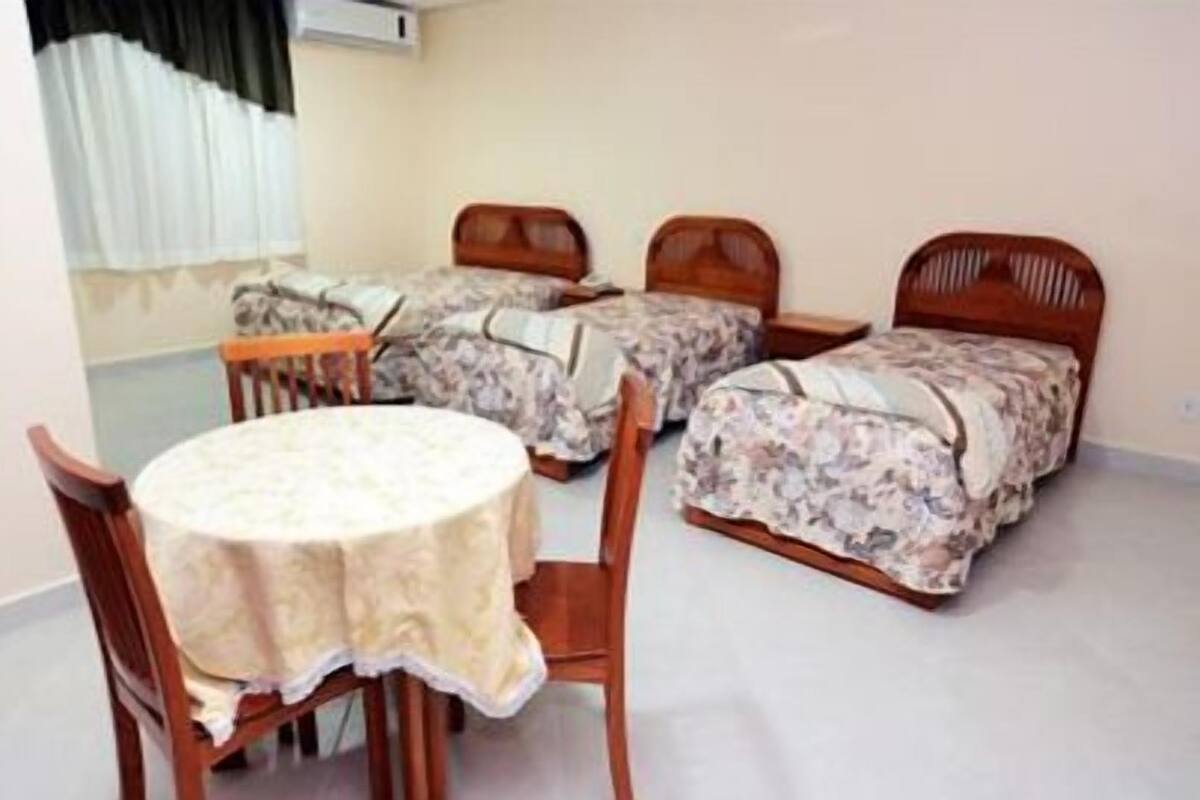 Une chambre avec deux lits simples, une table ronde avec des chaises et une fenêtre avec des rideaux.