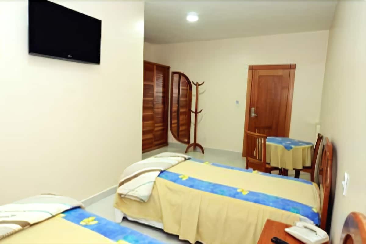 Une chambre d’hôtel avec deux lits, un bureau avec une chaise, une armoire et un téléviseur fixé au mur.