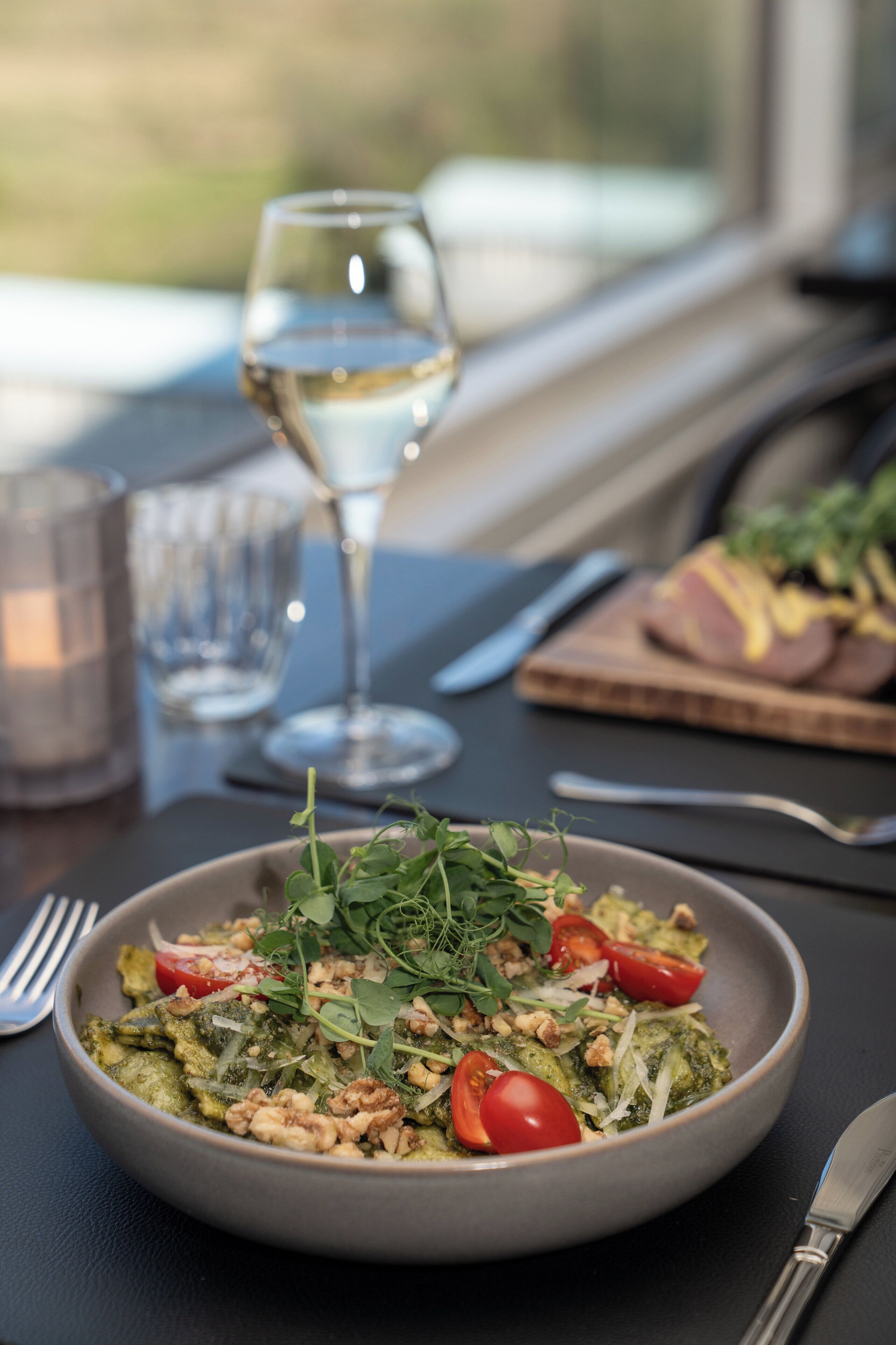 Insalata con pomodori, noci e verdure su un tavolo, insieme a un bicchiere di vino bianco e uno di acqua.