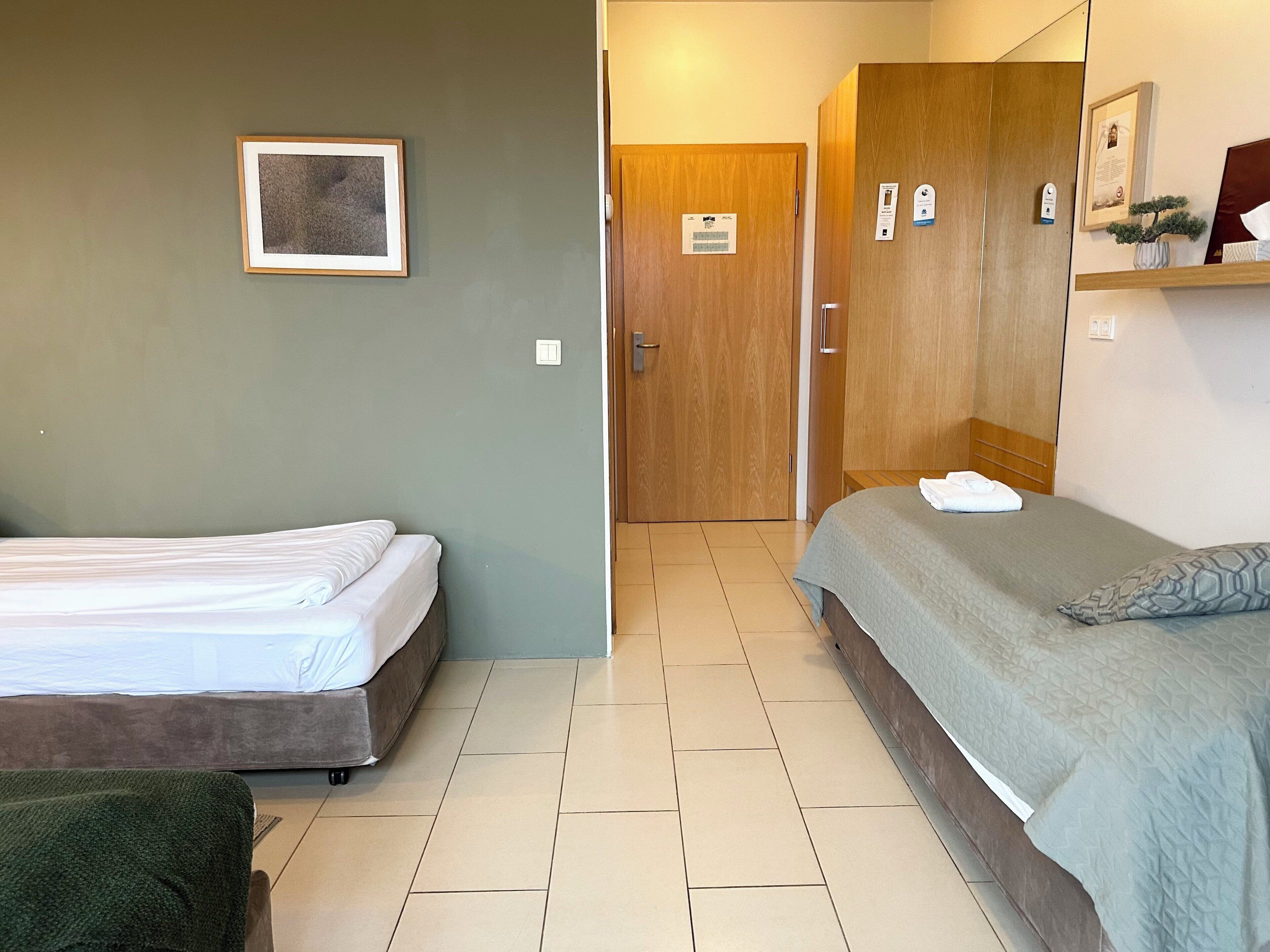 Une chambre d’hôtel avec deux lits, une armoire en bois, un tableau encadré au mur et une petite table avec une serviette.