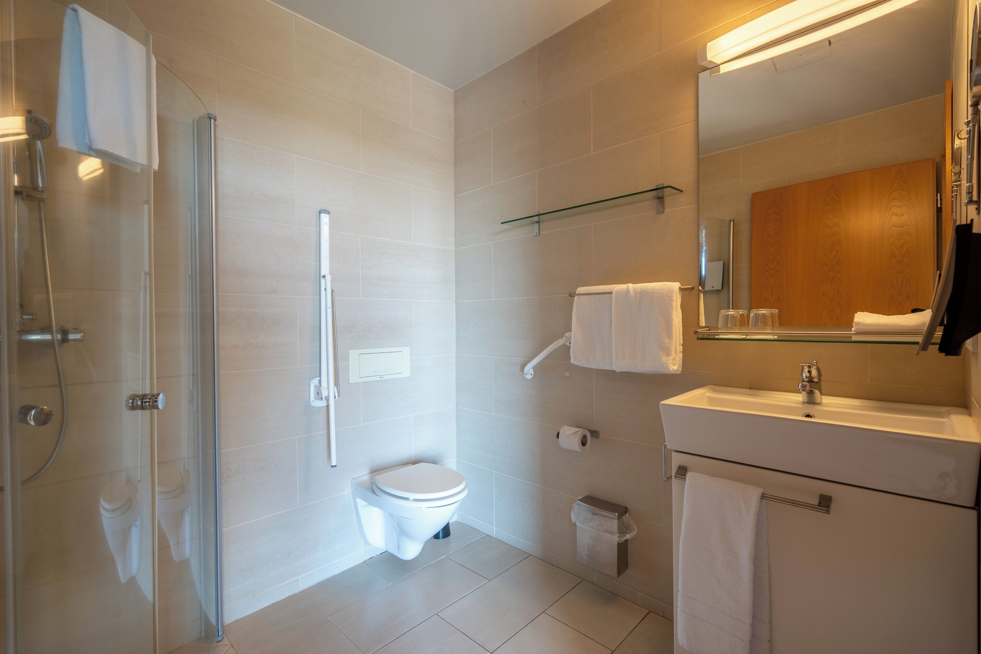 Un baño moderno con cabina de ducha de vidrio, inodoro, lavabo con espejo y perchero para toallas.