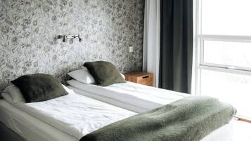 A double bed with a green throw blanket, a nightstand with a lamp, and a window with curtains.