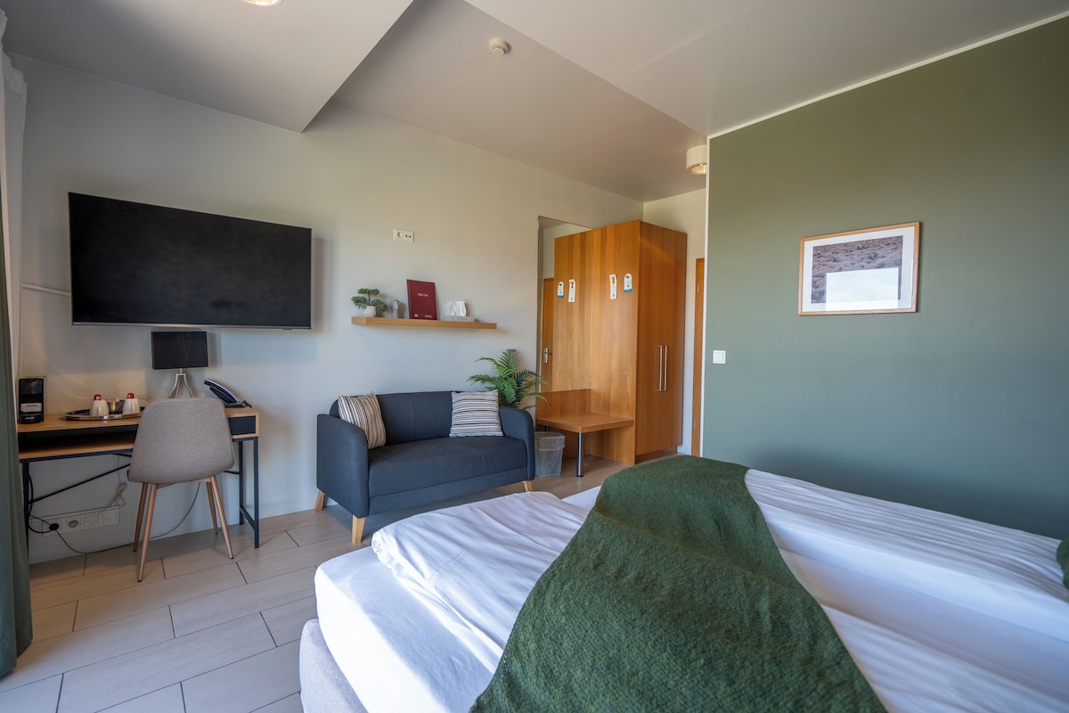 A modern hotel room with a bed, desk, chair, TV, and wardrobe.