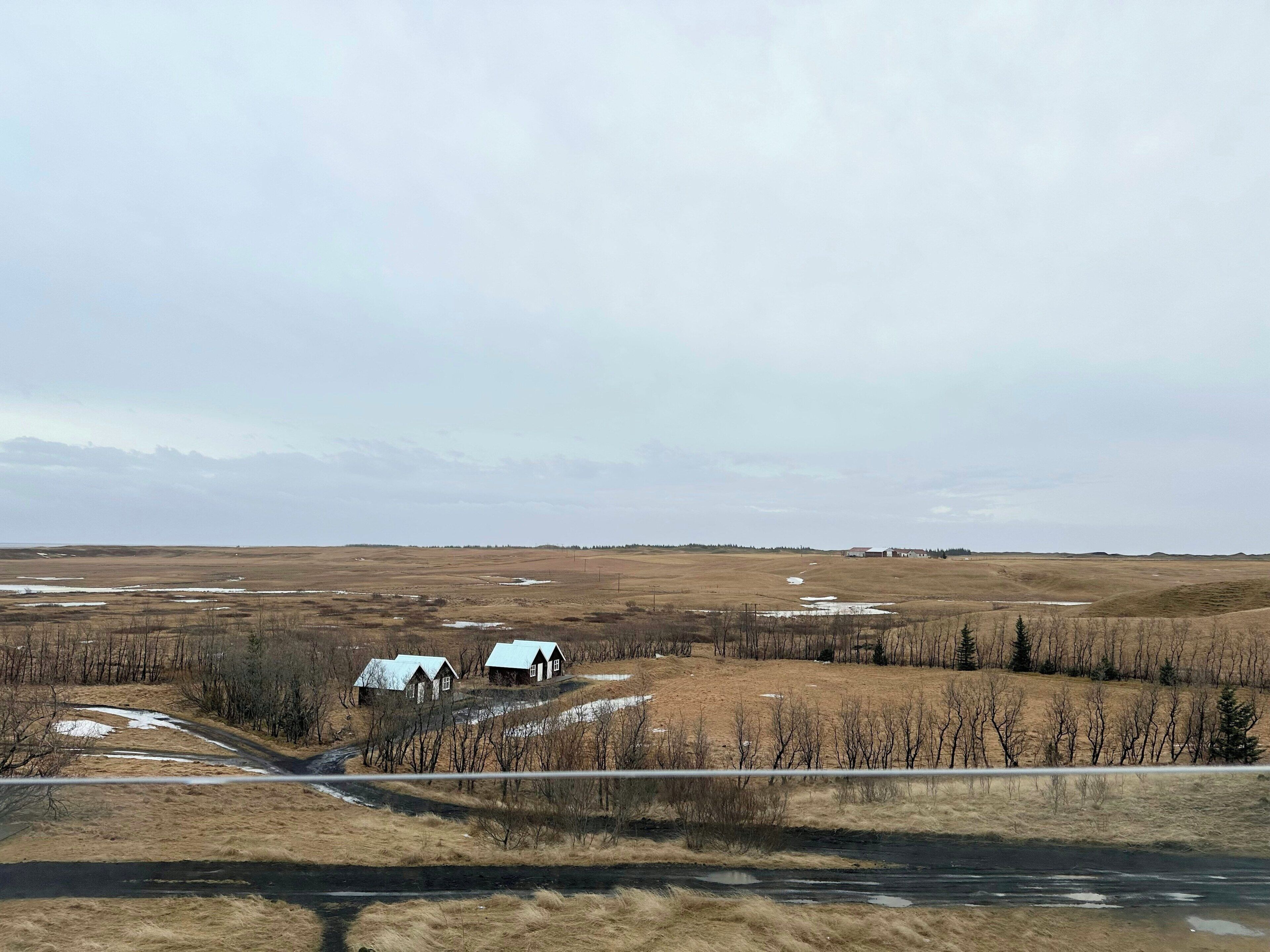 A rural landscape with a dirt road, two small houses, and a flat terrain.