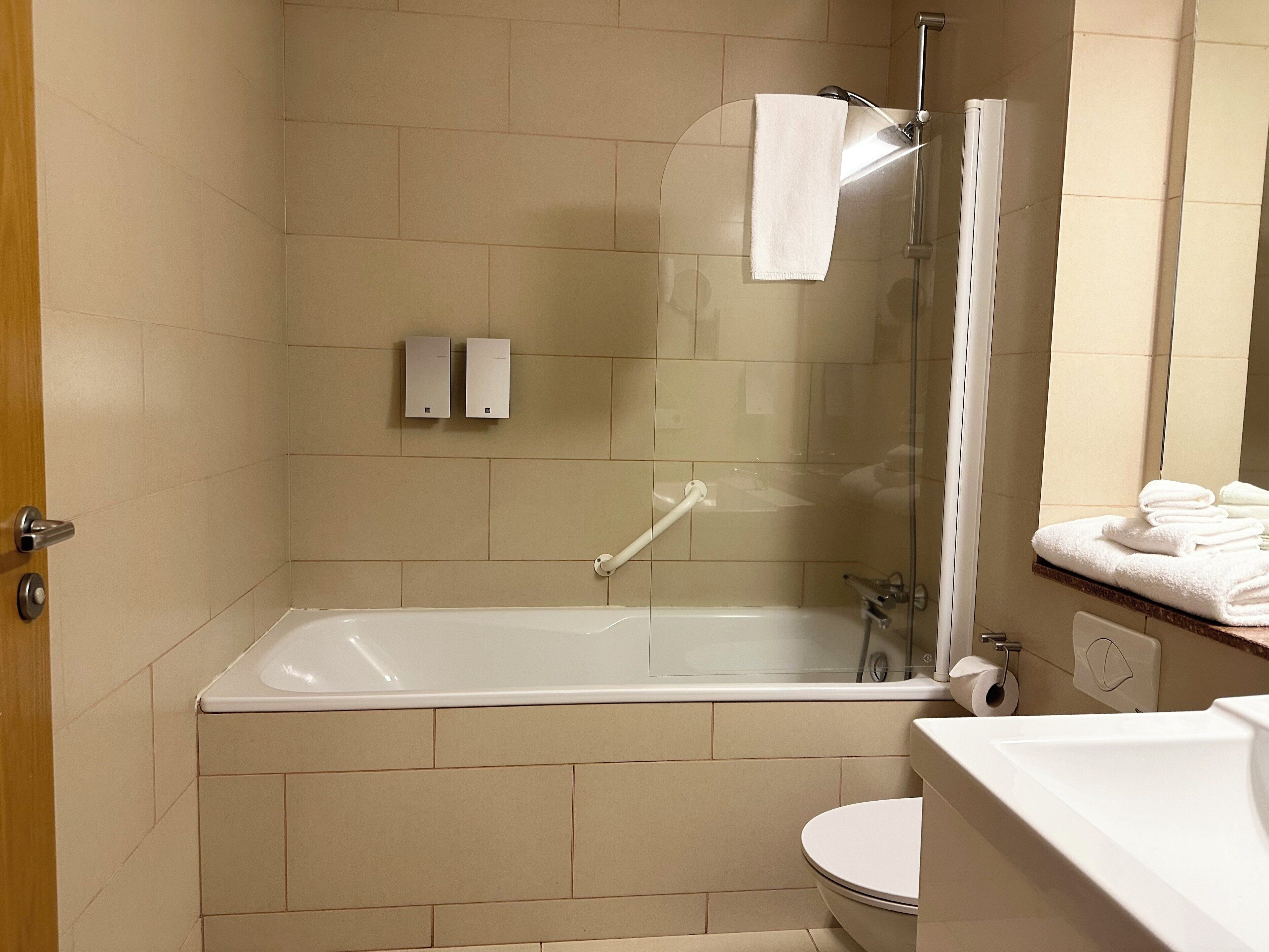 A modern bathroom with a glass-enclosed shower, a white bathtub, and a toilet.