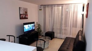 A living room with a TV, a sofa, a dining table, and a plant. - Depto en Iquique Ed. Terranova 1108 (Iquique)
