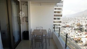 A balcony with a table and chairs, overlooking a cityscape with buildings and a road. - Depto en Iquique Ed. Terranova 1108 (Iquique)