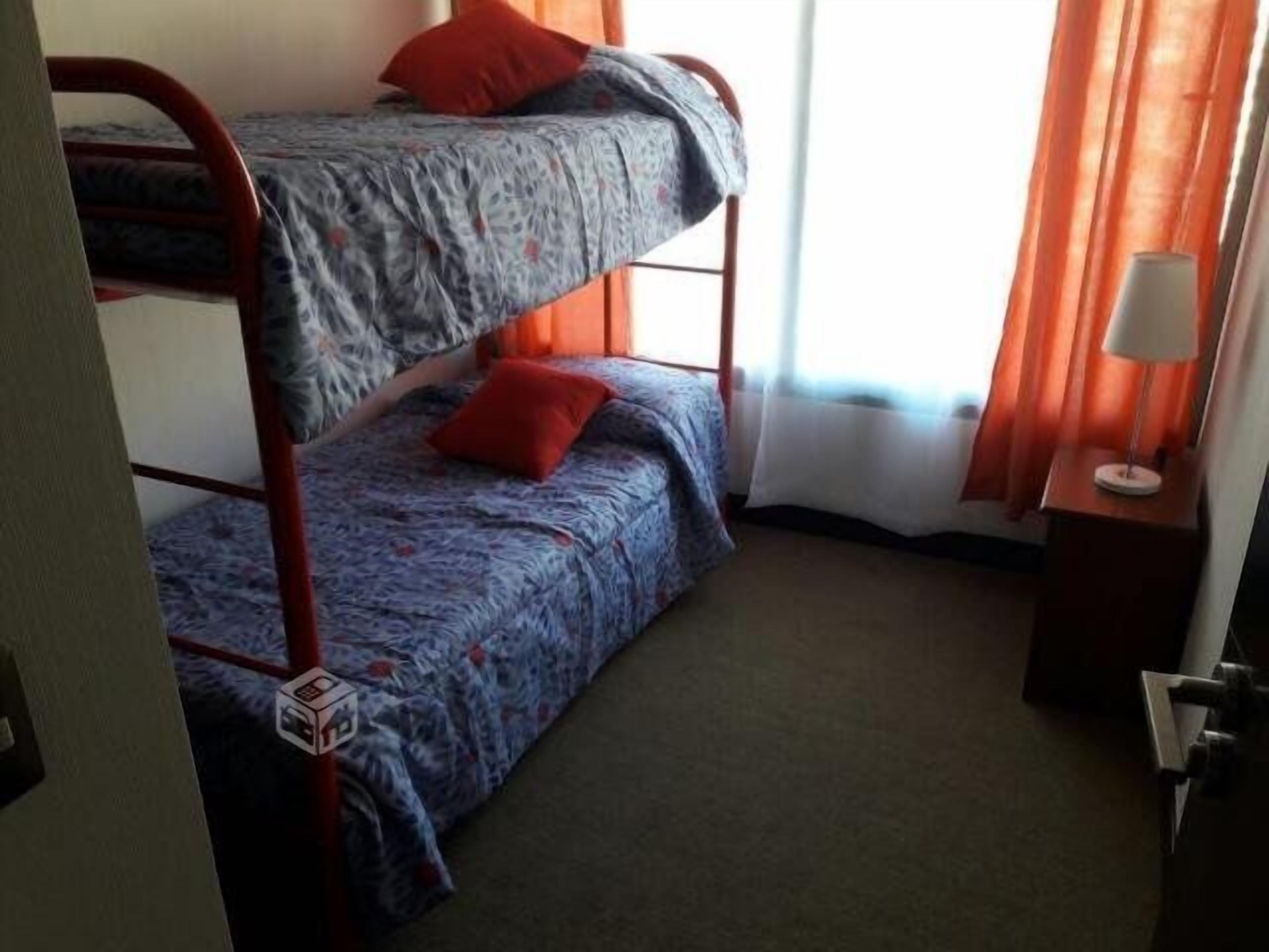 A bunk bed room with two beds, a nightstand with a lamp, and a window with curtains.