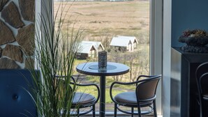 Un balcon avec un mur en pierre, une table ronde avec deux chaises, une plante en pot et une vue sur une maison située au loin.