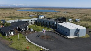 Un ensemble immobilier moderne comprenant un parking, un mât pour drapeau et offrant une vue sur un lac et des montagnes en arrière-plan.