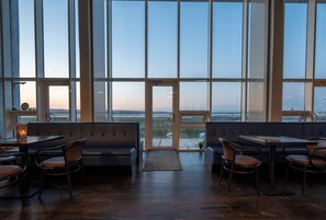 Un restaurant offrant une vue sur l’océan, avec une grande fenêtre, une table en bois et un banc.
