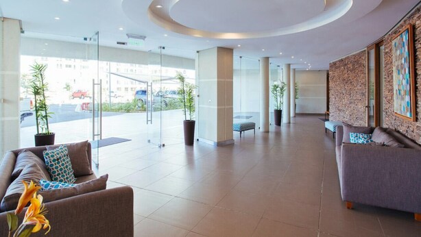 A spacious lobby with a modern design, featuring a curved ceiling, large windows, and a seating area with sofas and a bench. - Depto Euro Marina La Serena 1135 (Coquimbo)