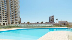 A swimming pool with a tiled deck, surrounded by a tall residential building and a smaller structure in the background. - Depto Euro Marina La Serena 1135 (Coquimbo)