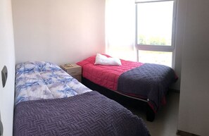 A bedroom with two beds, a nightstand, and a window with a view. - Depto Euro Marina La Serena 1135 (Coquimbo)
