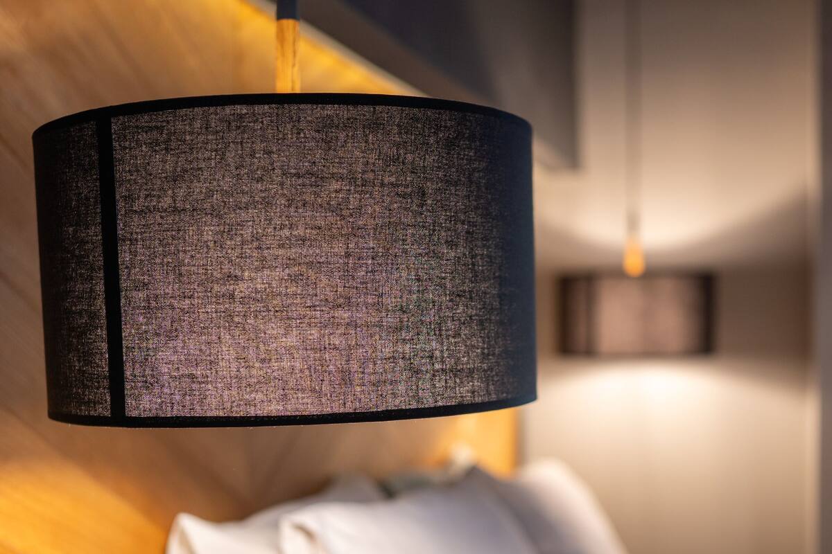 A modern bedroom with a wooden headboard, a hanging lamp, and a neatly made bed with white linens.