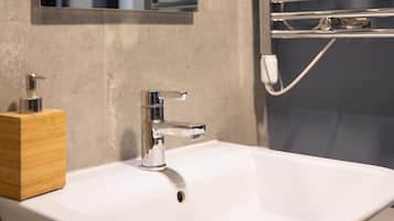 Un baño con lavamanos blanco, un espejo y un perchero con una toalla.