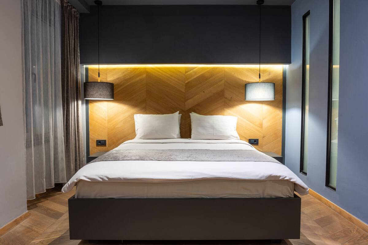 A modern bedroom with a large bed, wooden headboard, and two bedside lamps.