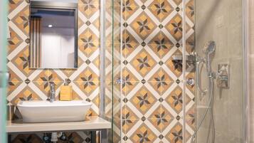 A bathroom with a glass-enclosed shower, a sink with a mirror above it, and patterned tiles on the walls.