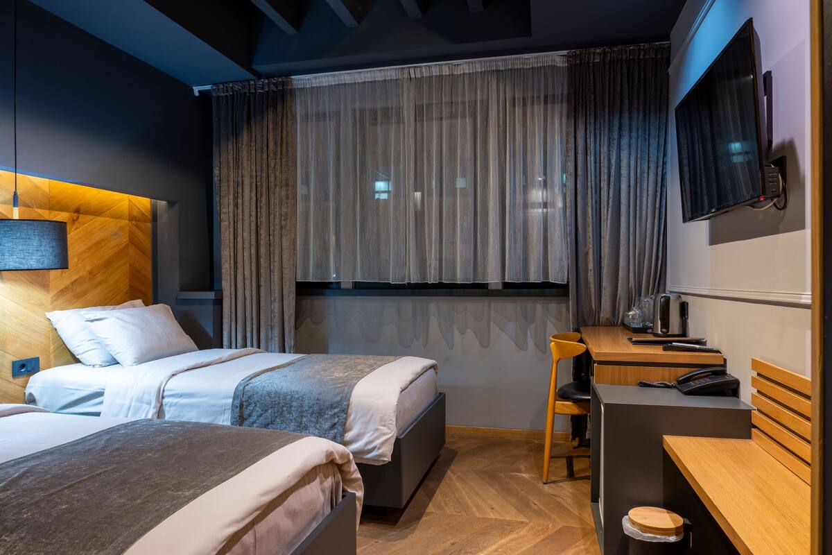 A hotel room with two beds, a desk, a chair, a TV, and a window with curtains.