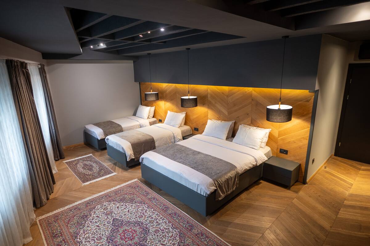 A modern bedroom with three beds, a herringbone-patterned wooden wall, and a large patterned rug.