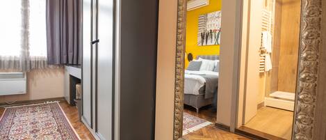A hotel room with a large mirror, a bed with a gray headboard, a wooden floor, and a window with curtains.