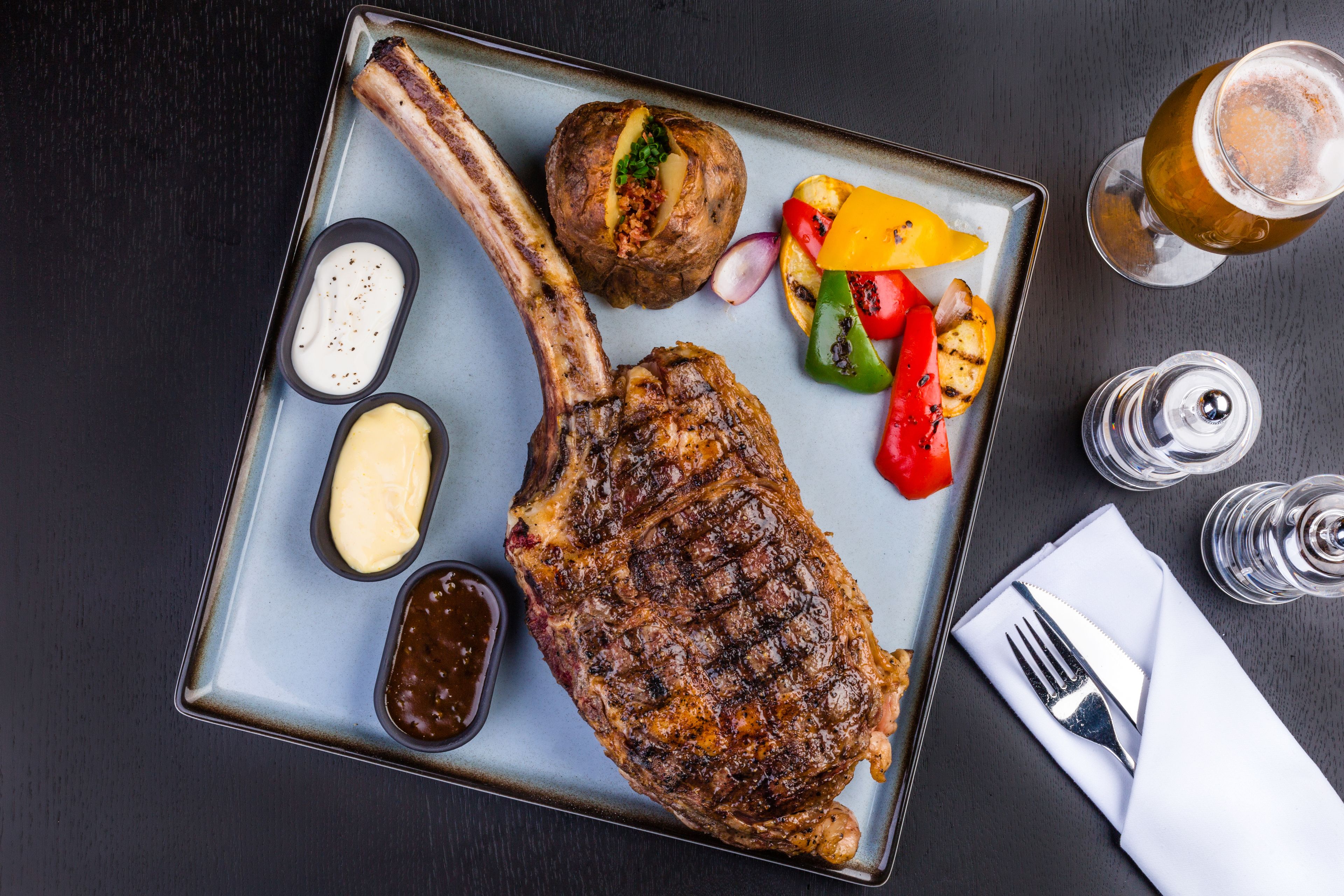 A steak with a side of vegetables and sauces on a plate.